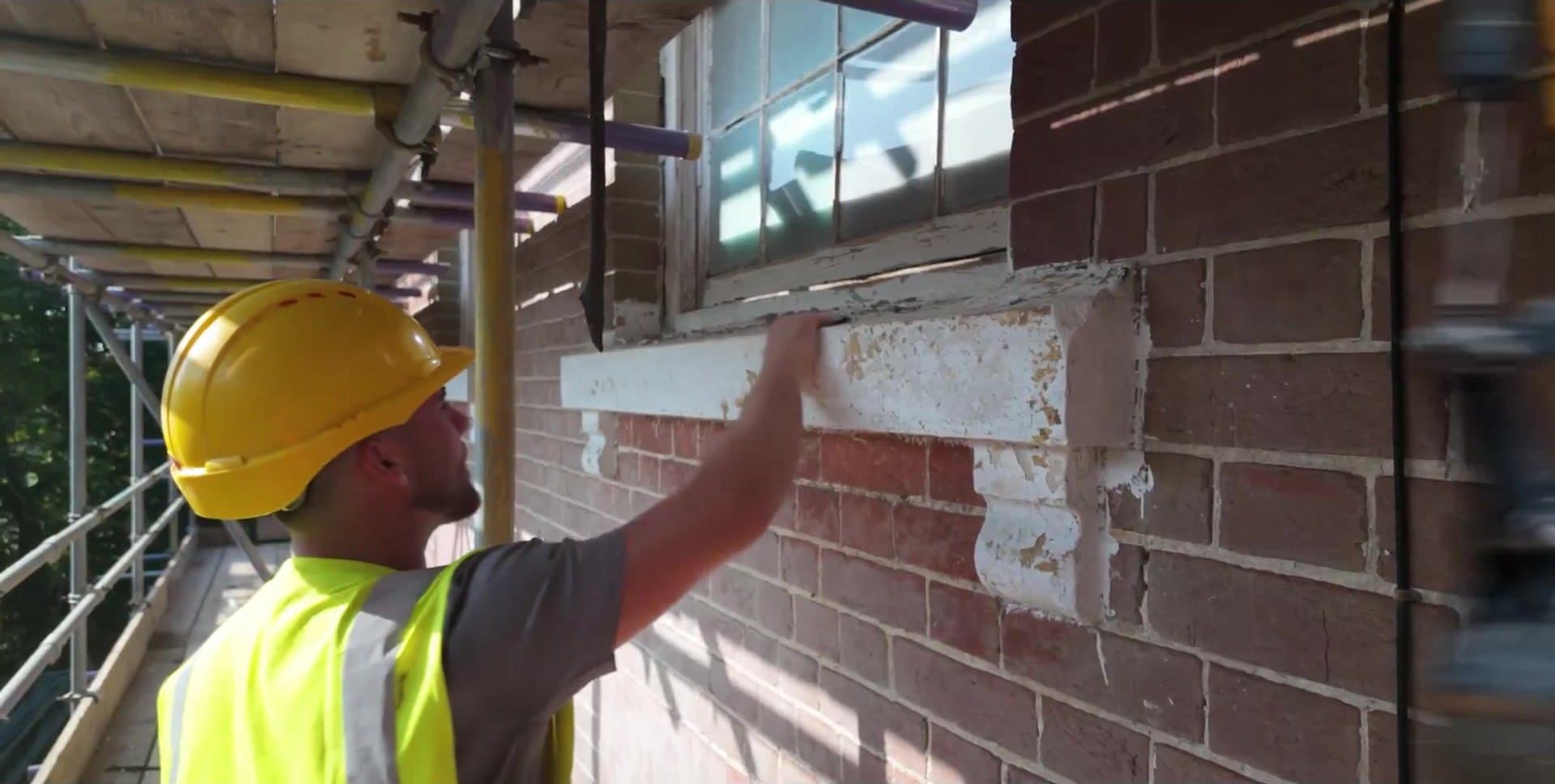 A Colver tradesman in a hard hat repairing brickwork beneath a window